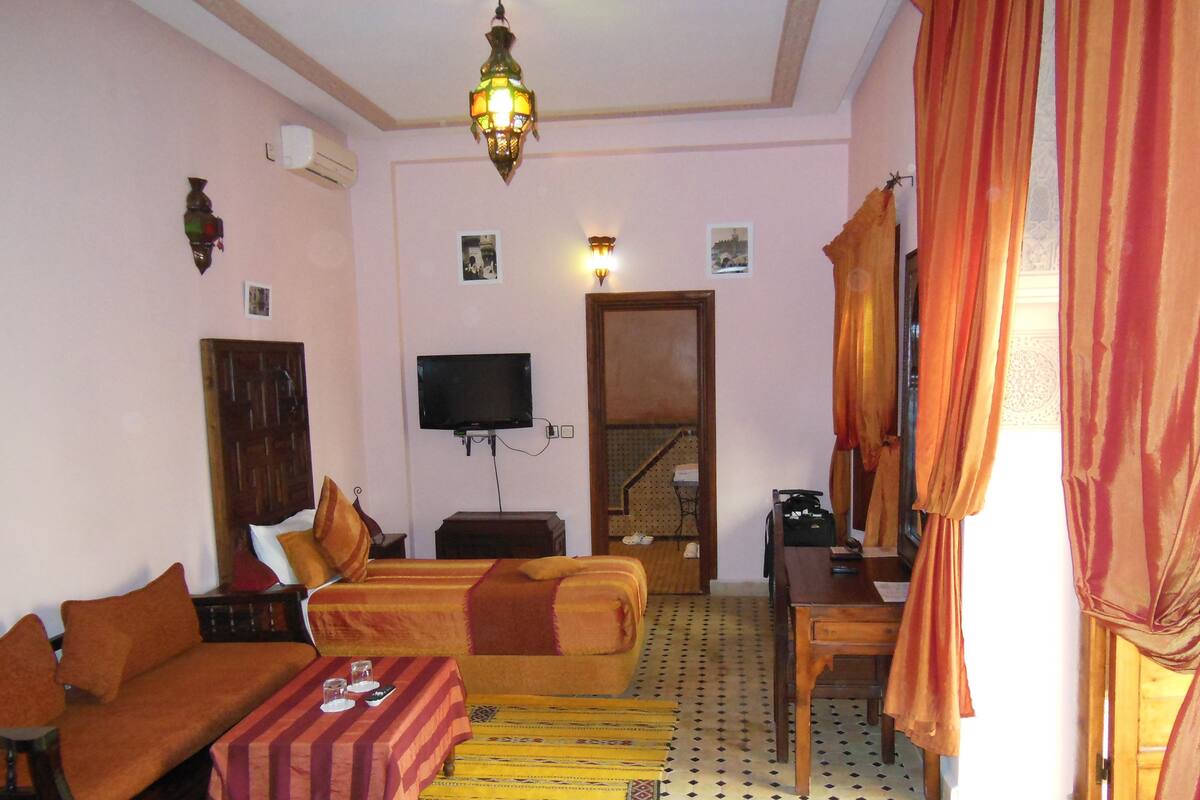 A hotel room with a sofa, a bed, a desk, a television, and a staircase leading to an upper floor.