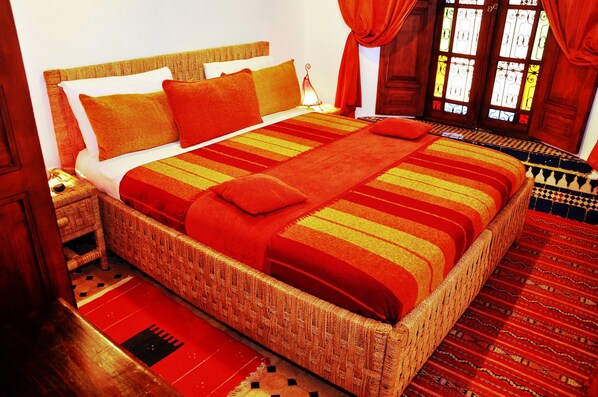 Una cama grande con cabecera trenzada, ropa de cama a rayas rojas y amarillas, y una manta roja.