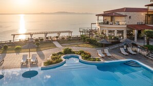 A pool area with lounge chairs, a pool, and a view of the sea at sunset. - Blue Bay Halkidiki “Adults Only ” (Kassandra)