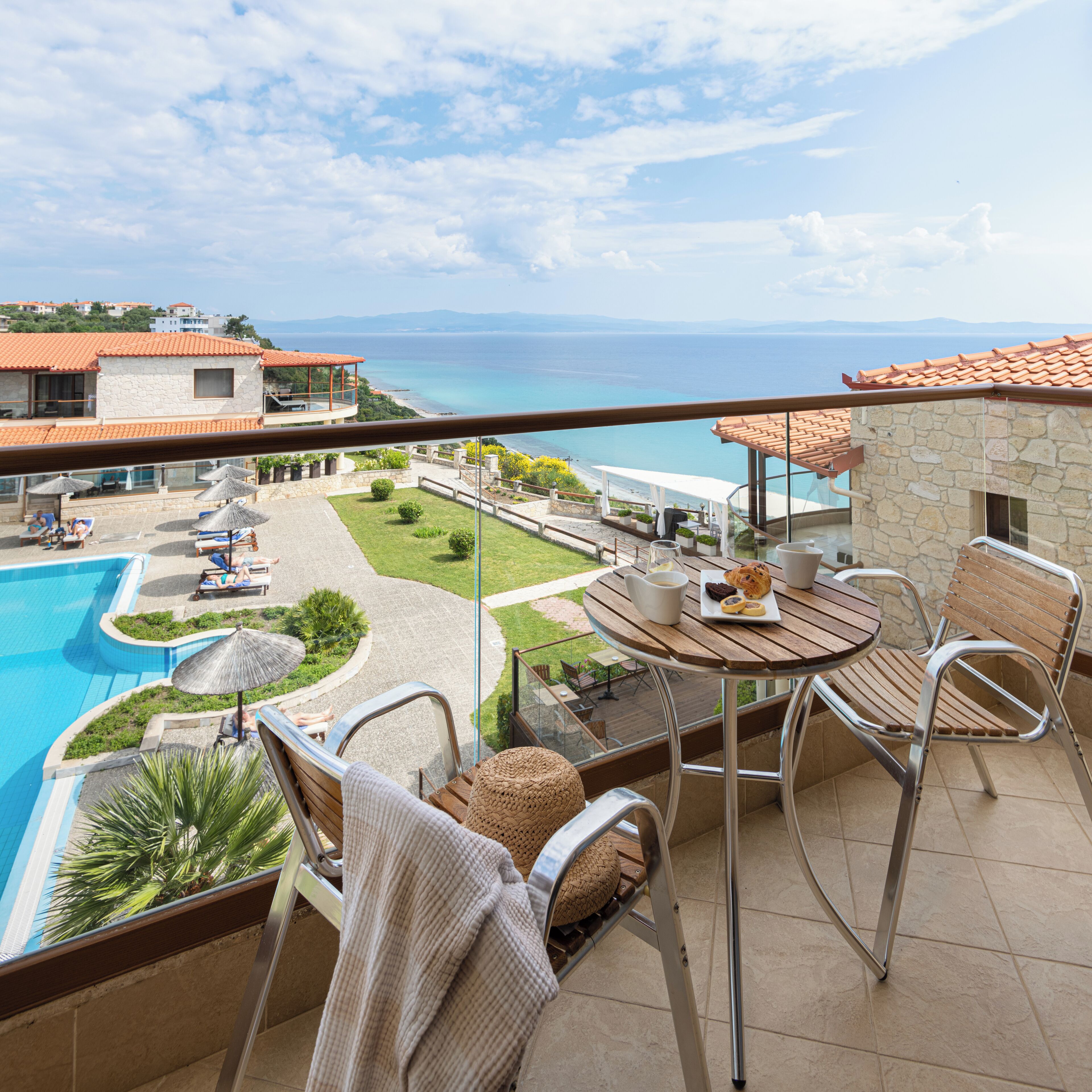 Ein Balkon mit Blick auf einen Swimmingpool, ein Essbereich mit Tisch und Stühlen sowie ein Steinhaus mit rotem Ziegeldach.