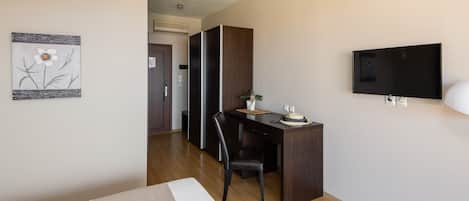 A hotel room with a bed, a desk with a chair, a television, and a door leading to a bathroom.