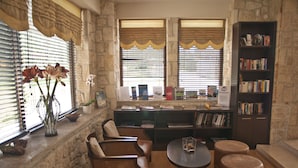 A cozy reading nook with a stone wall, a bookshelf, comfortable seating, and a window with blinds. - Blue Bay Halkidiki “Adults Only ” (Kassandra)