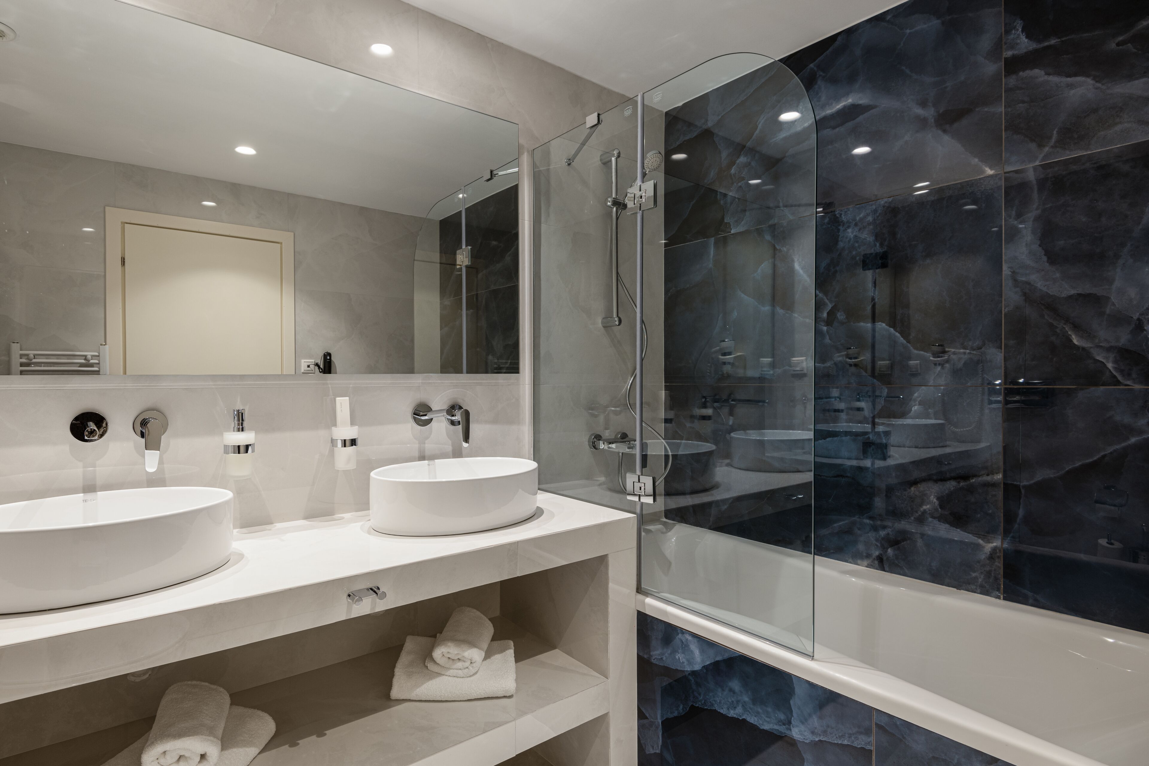 A modern bathroom with two sinks, a glass-enclosed shower, and a large mirror.