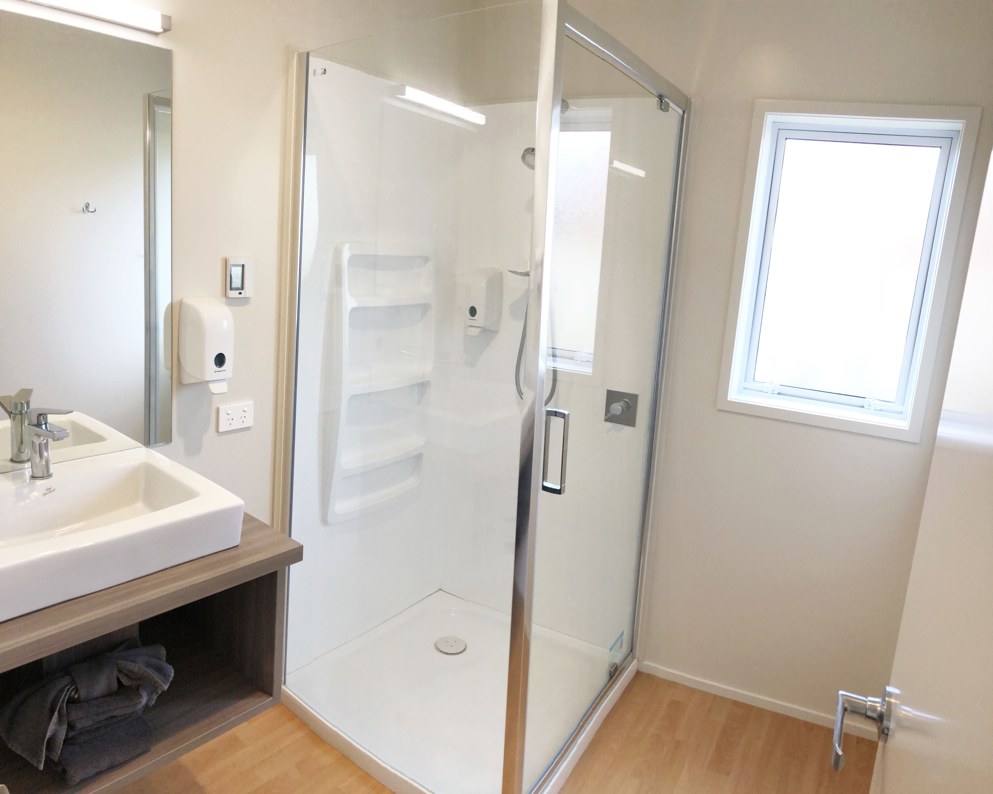 Un baño con ducha de vidrio, un lavamanos con espejo y una ventana.