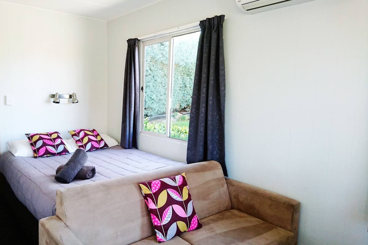 A room with two beds, a sofa, a window with curtains, and an air conditioning unit.