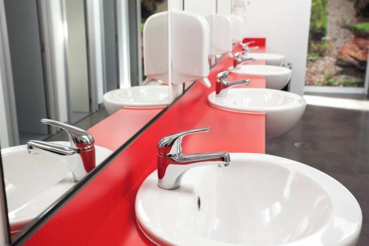 A modern bathroom with three white sinks and chrome faucets, a red countertop, and a large mirror.