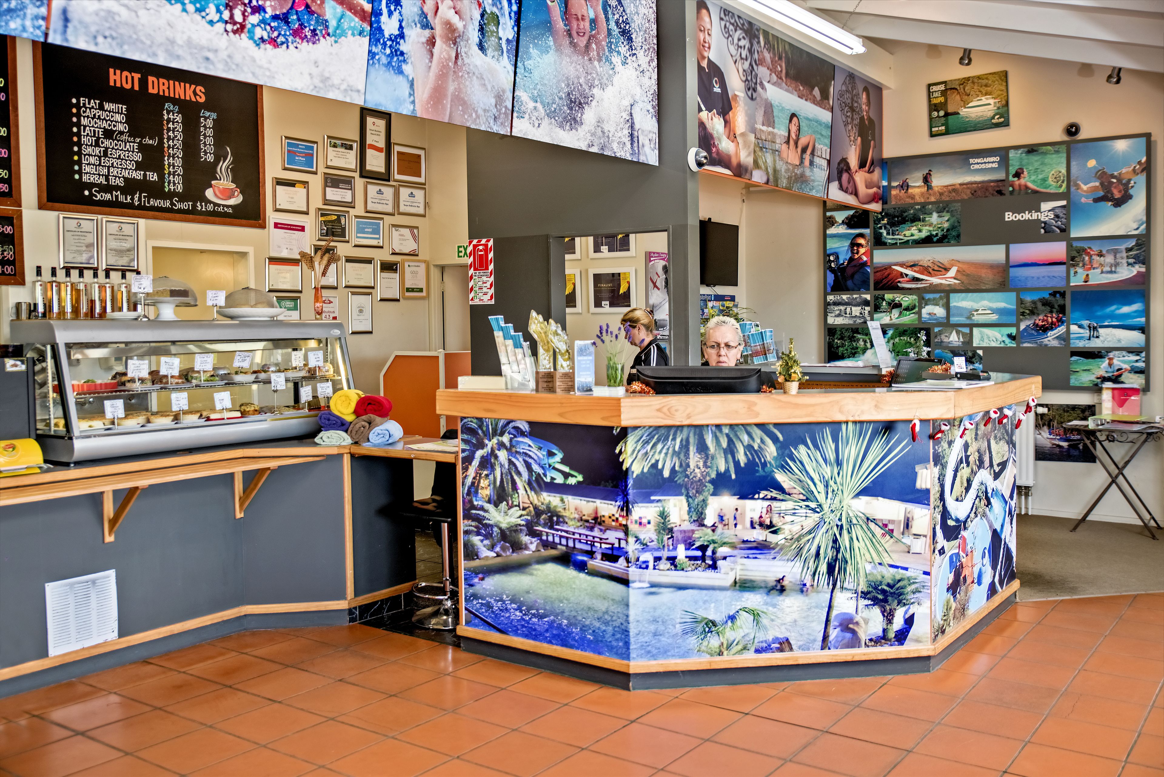 A coffee shop interior with a counter displaying various drinks, a menu above the counter, and a wall decorated with travel photos.