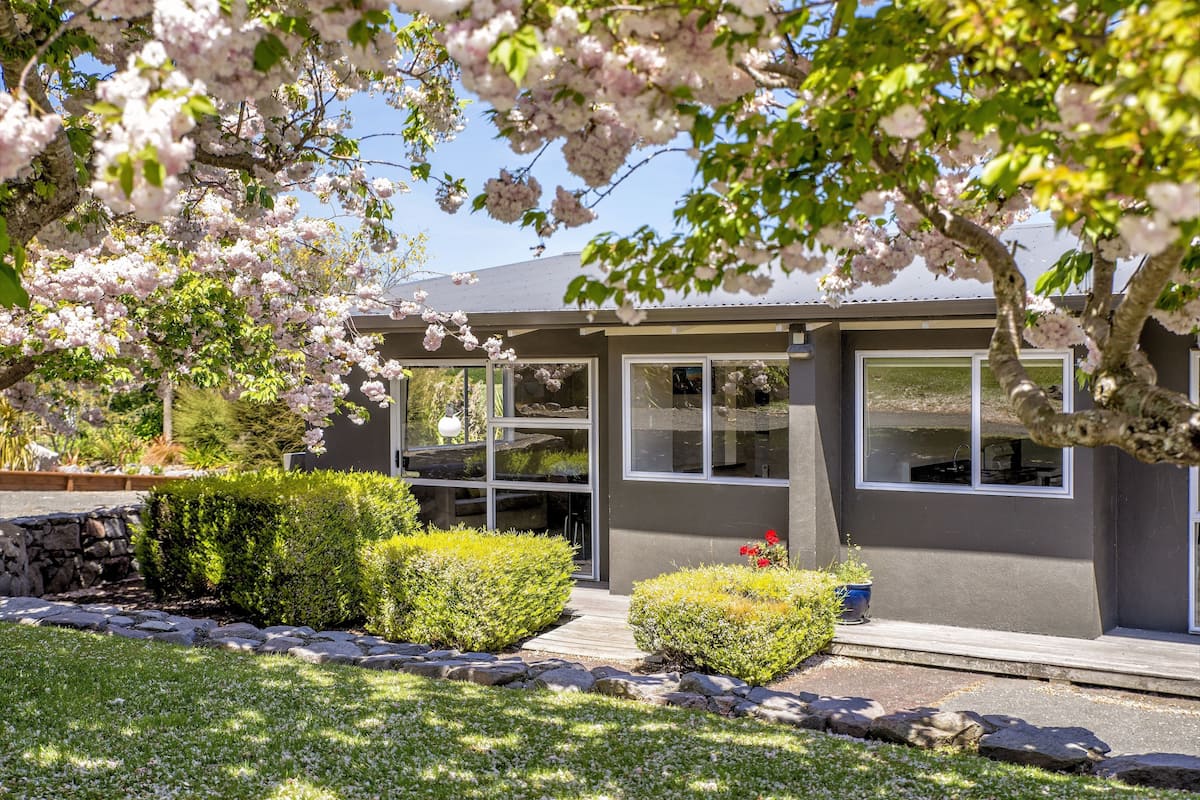 A modern house with a stone wall, a well-maintained lawn, and flowering trees.