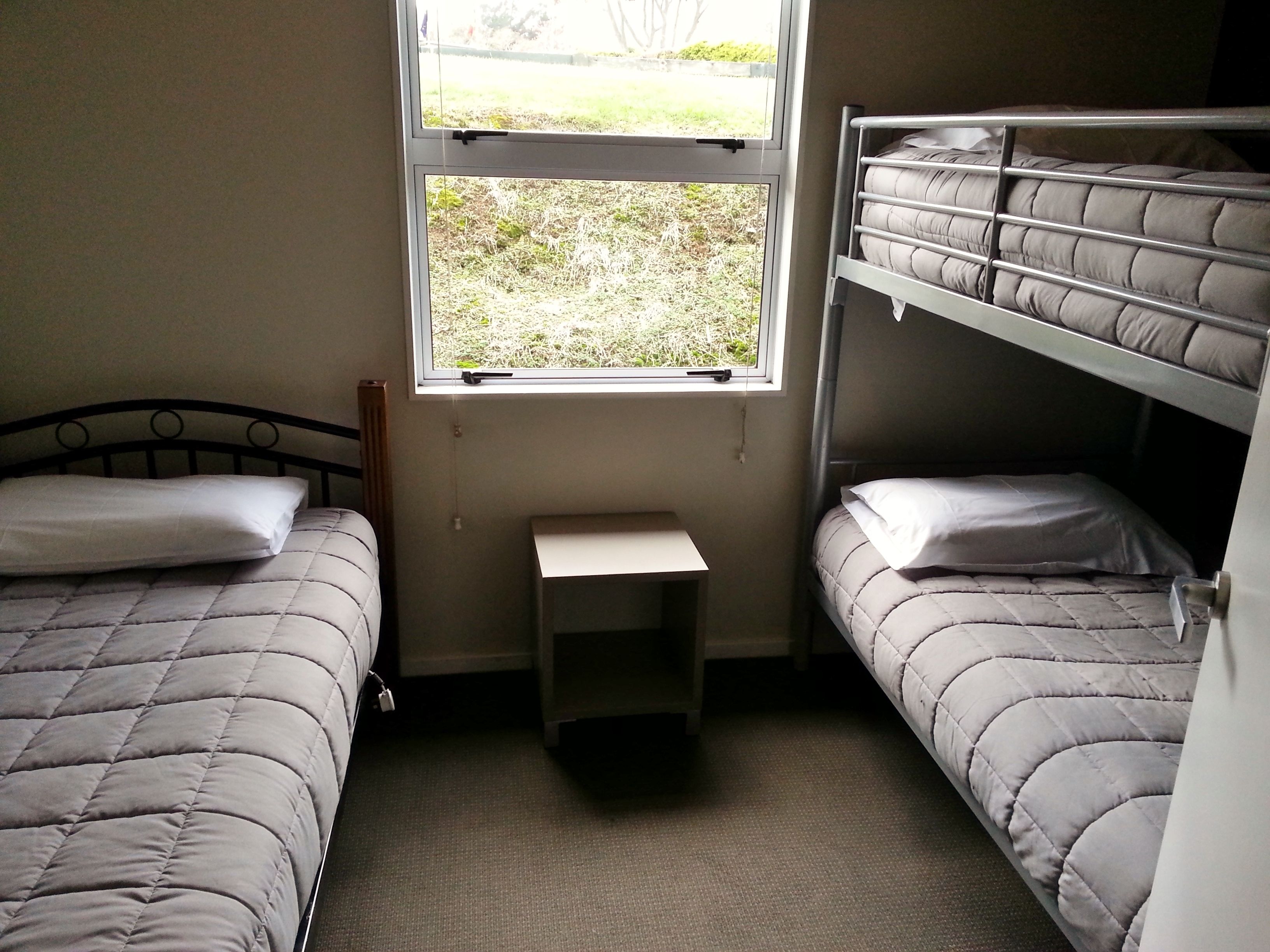 Habitación tipo dormitorio con dos camas individuales, una mesita pequeña y una ventana con vistas a zonas verdes.