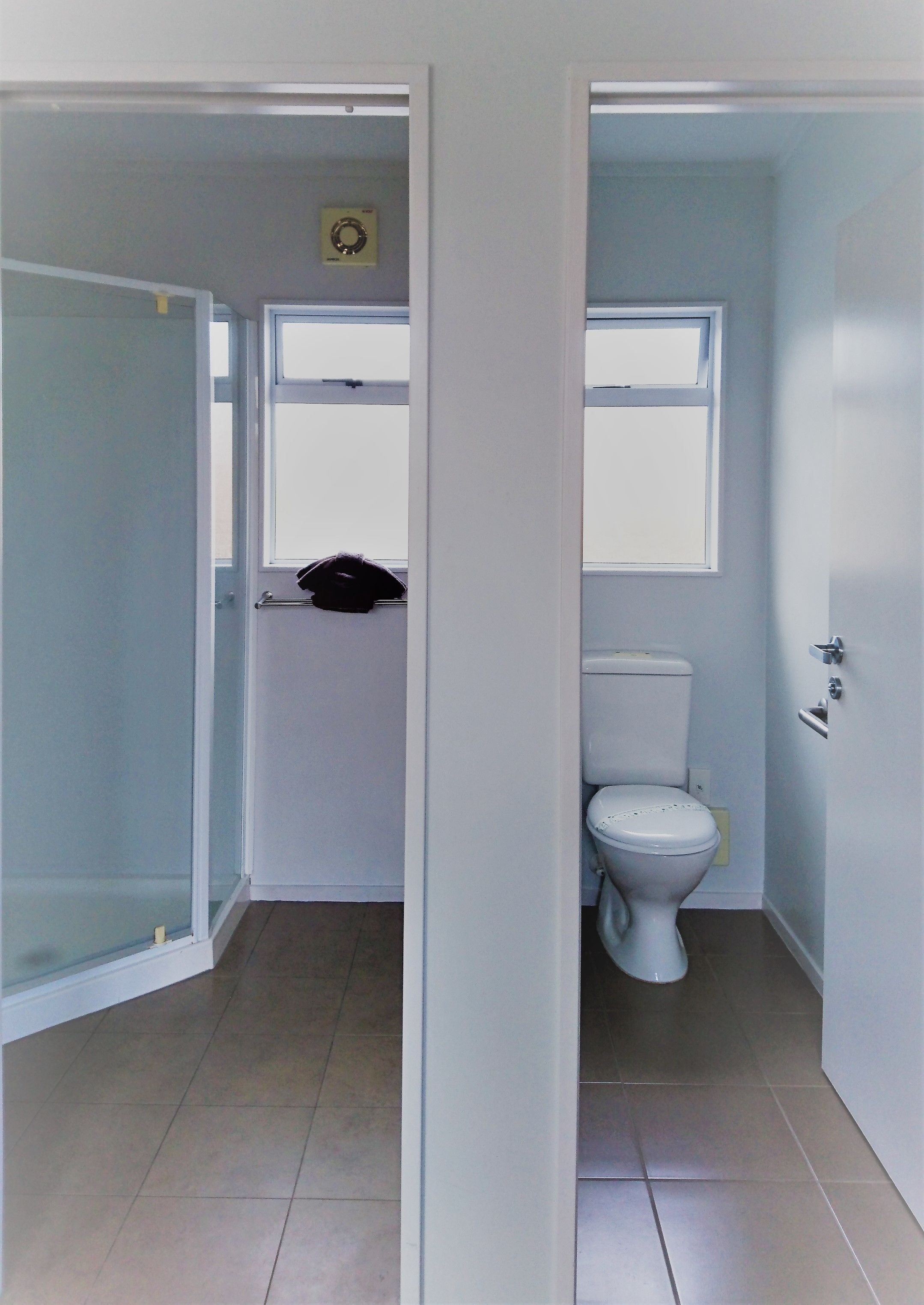 Un couloir étroit mène à une salle de bain équipée de toilettes et d’une fenêtre.