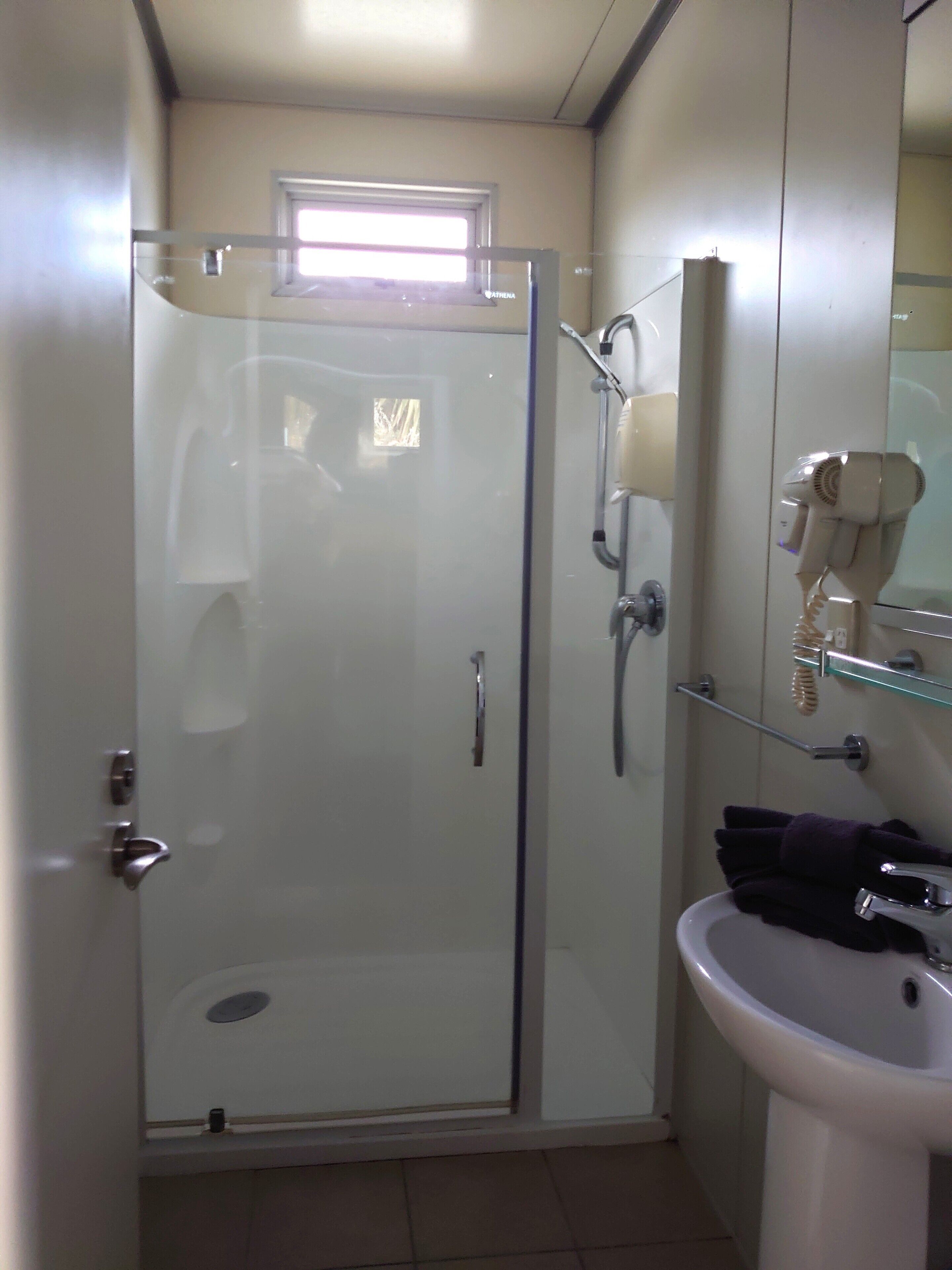Un baño con cabina de ducha de vidrio, un lavamanos y un secador de pelo en un estante.