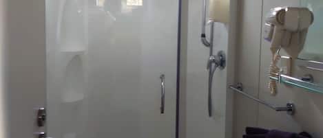 Un baño con cabina de ducha de vidrio, un lavamanos y un secador de pelo en un estante.