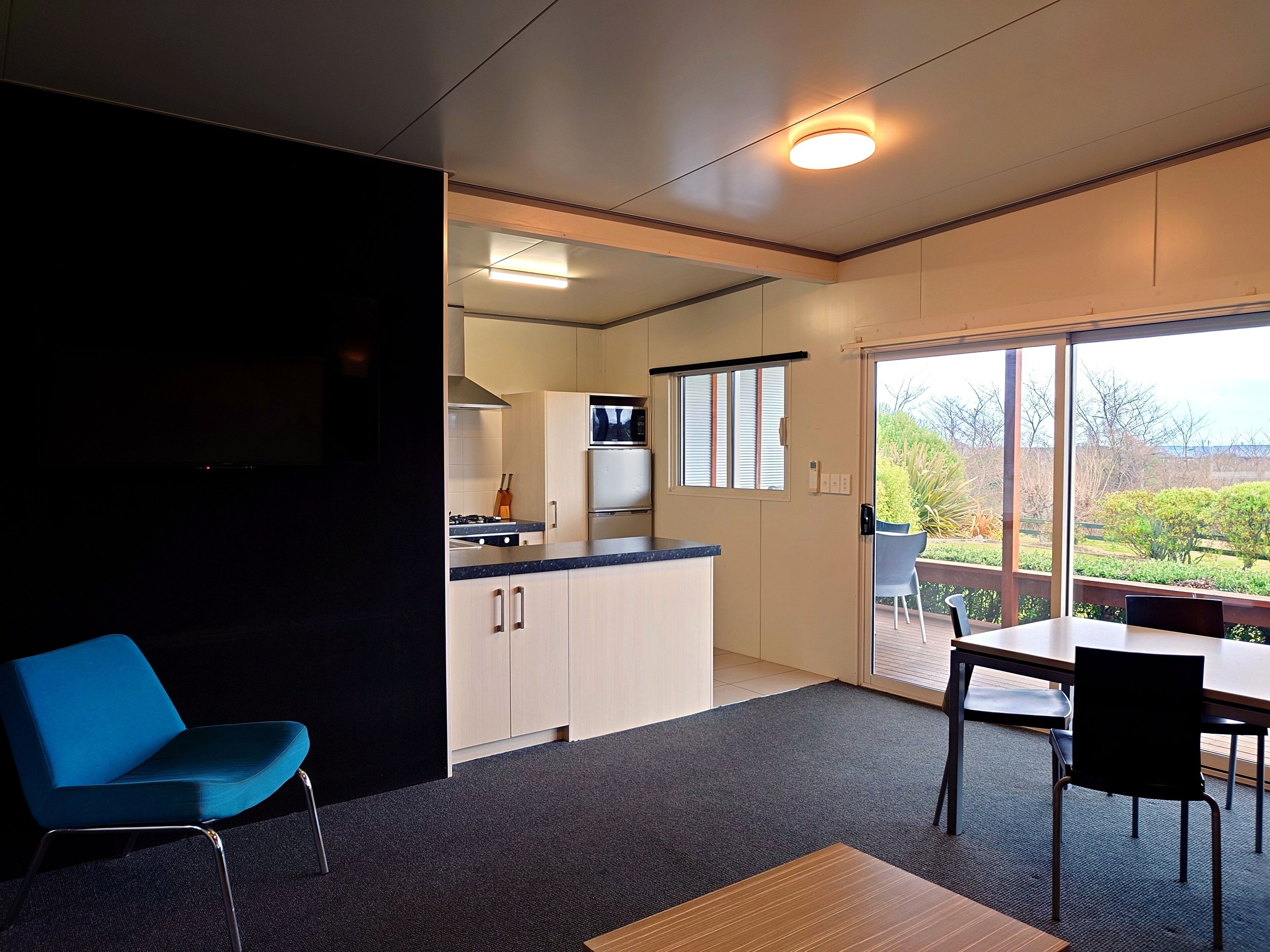 A modern kitchen with a dining area, a blue chair, and a view through a large window.