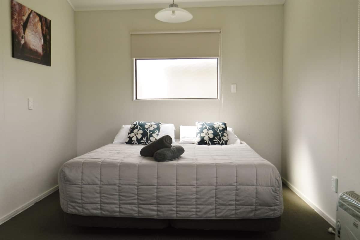 A bedroom with a bed, pillows, a blanket, a radiator, and a window.