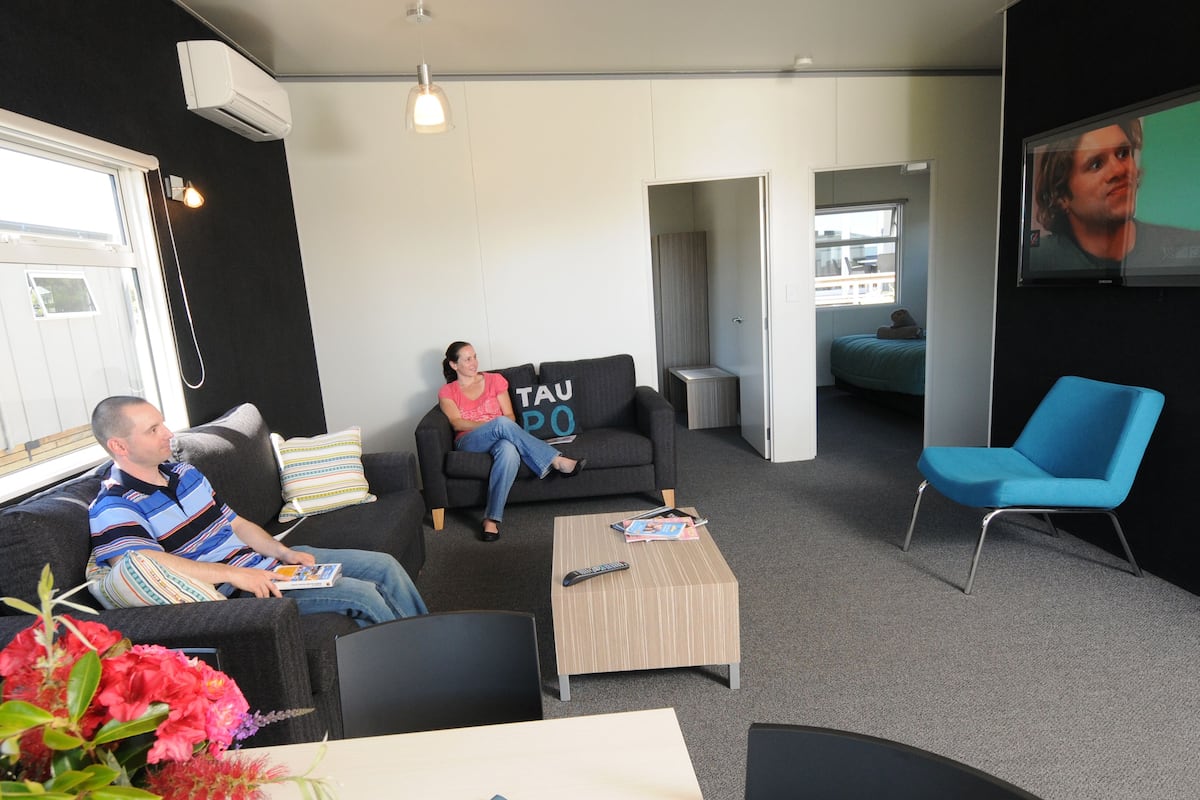 A modern living room with a sofa, a blue chair, and a coffee table. There is a TV mounted on the wall.