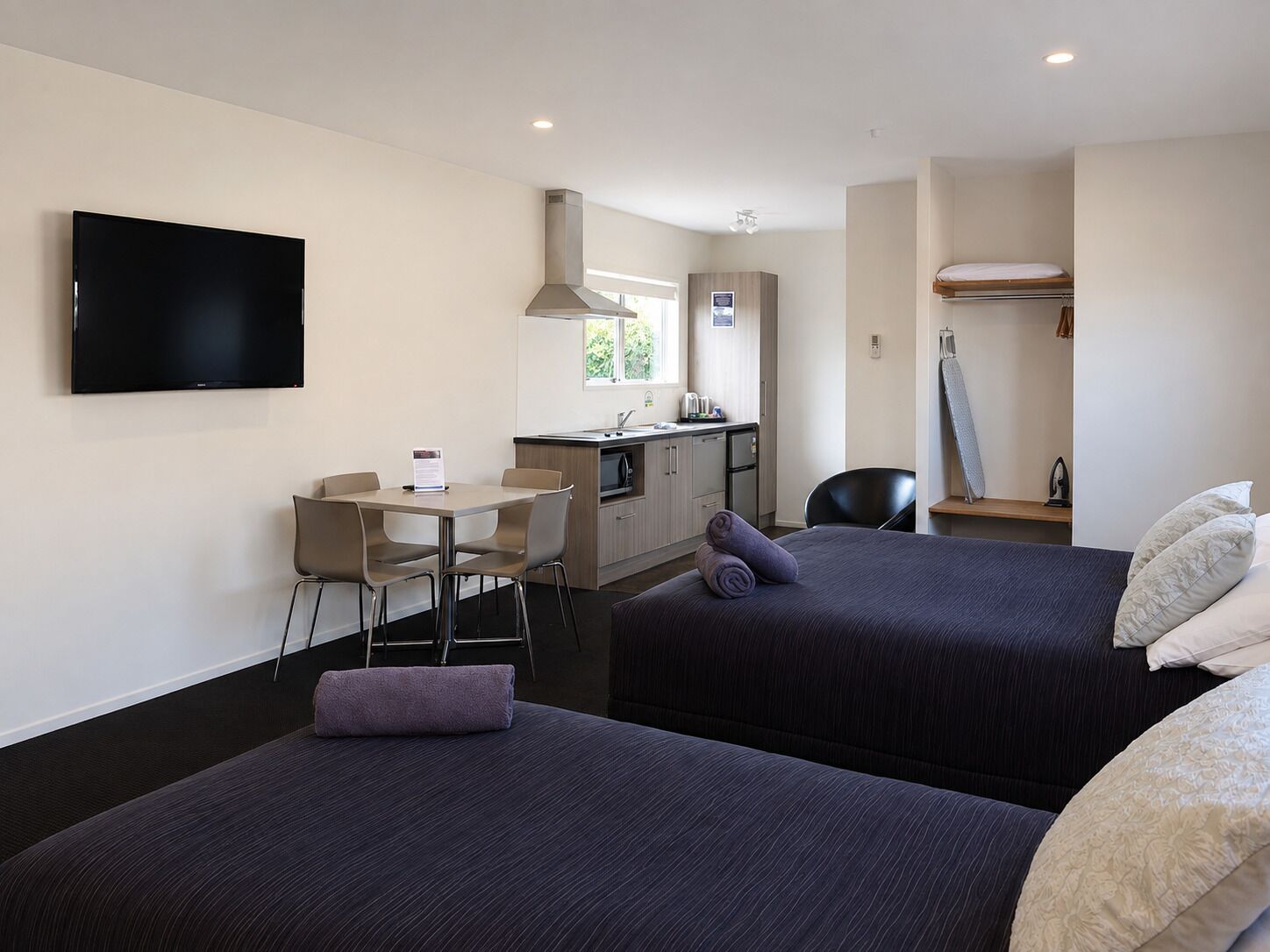 Habitación de hotel con dos camas, un escritorio, una silla, un televisor y una kitchenette.