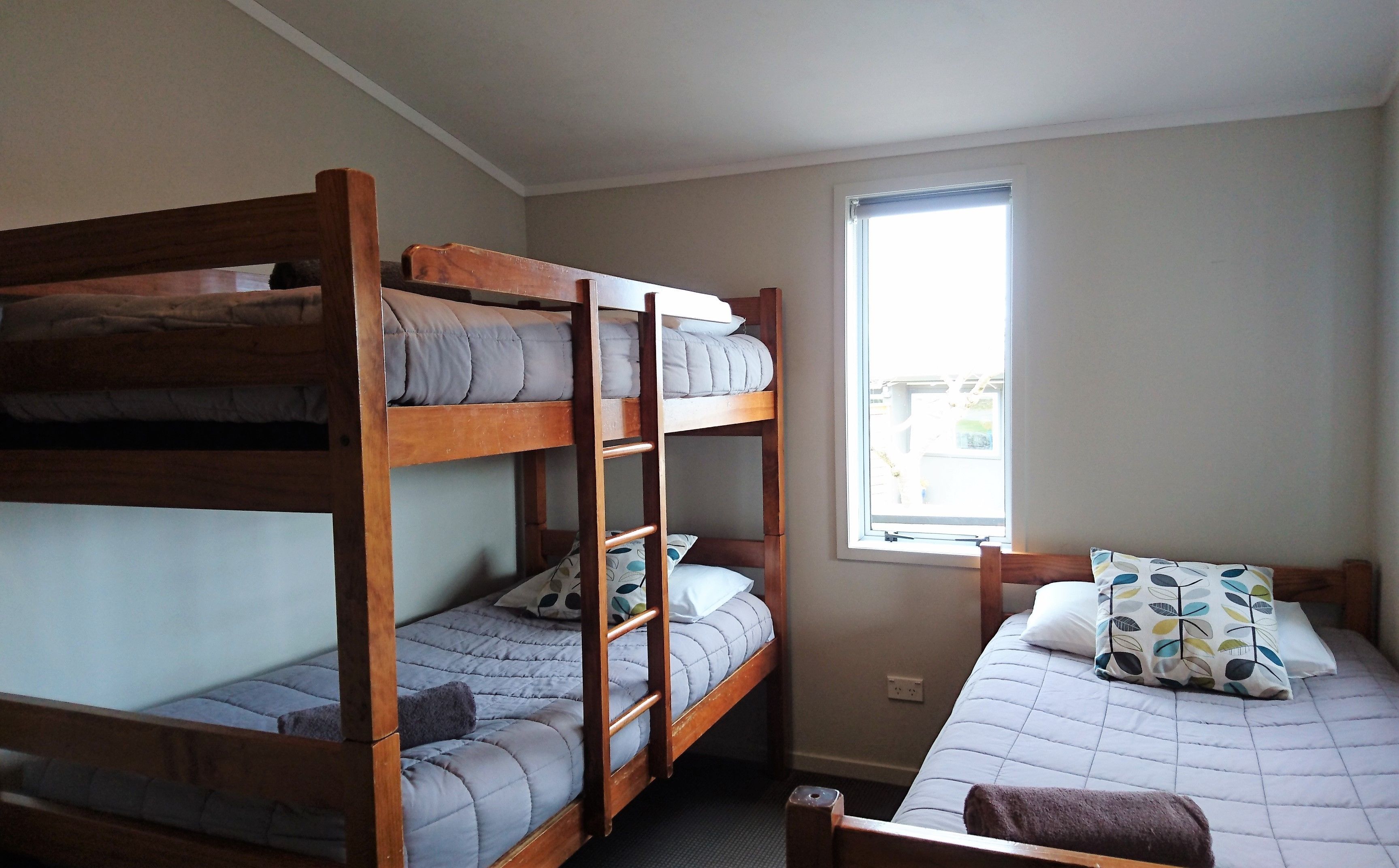 A dormitory room with bunk beds, a window, and a bed with a patterned pillow.