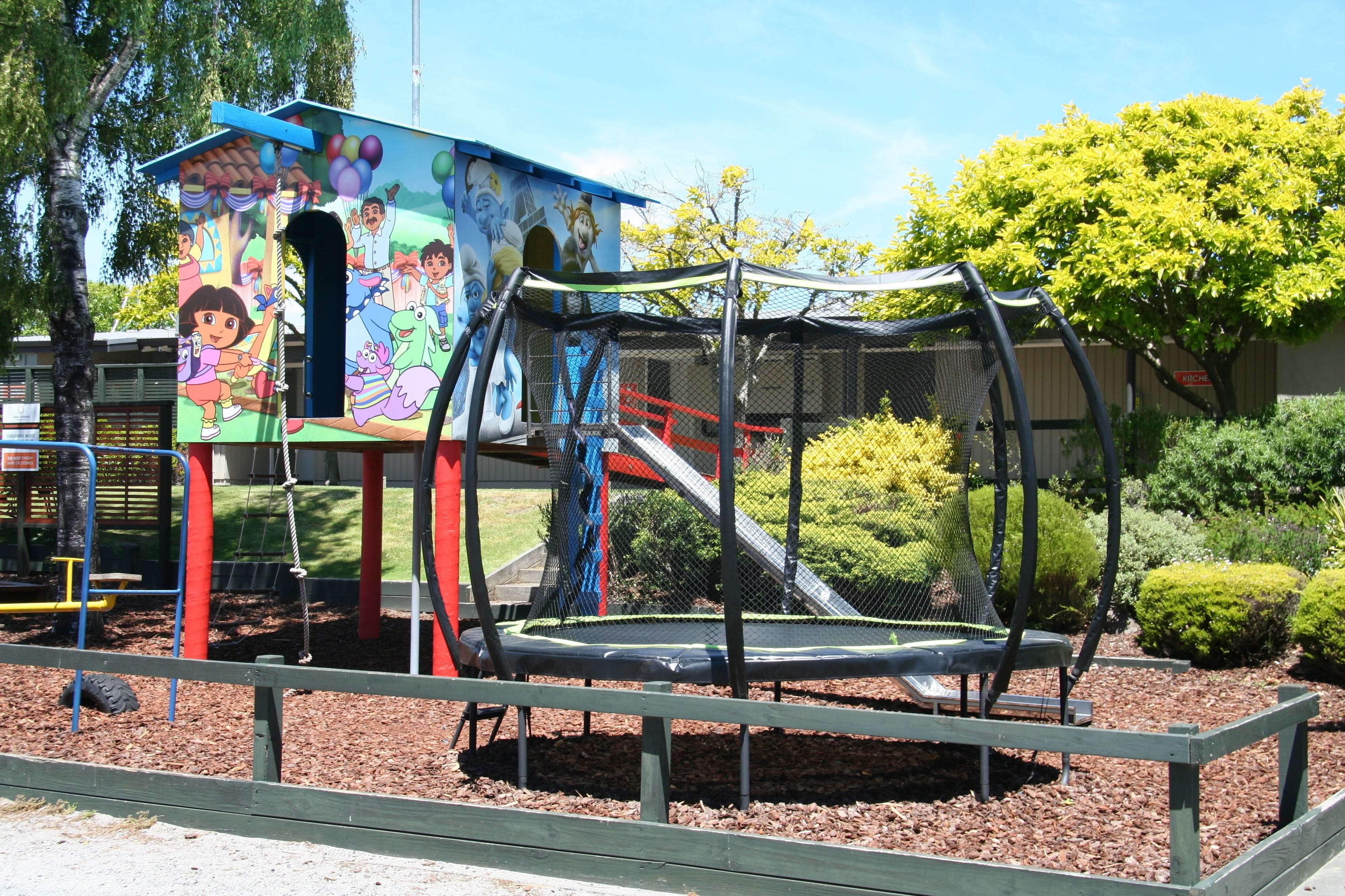 Un parque infantil con un trampolín, toboganes y un mural colorido en un edificio.