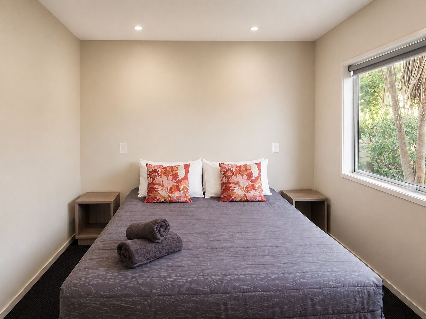 A bedroom with a bed, two pillows, a window, and a nightstand.
