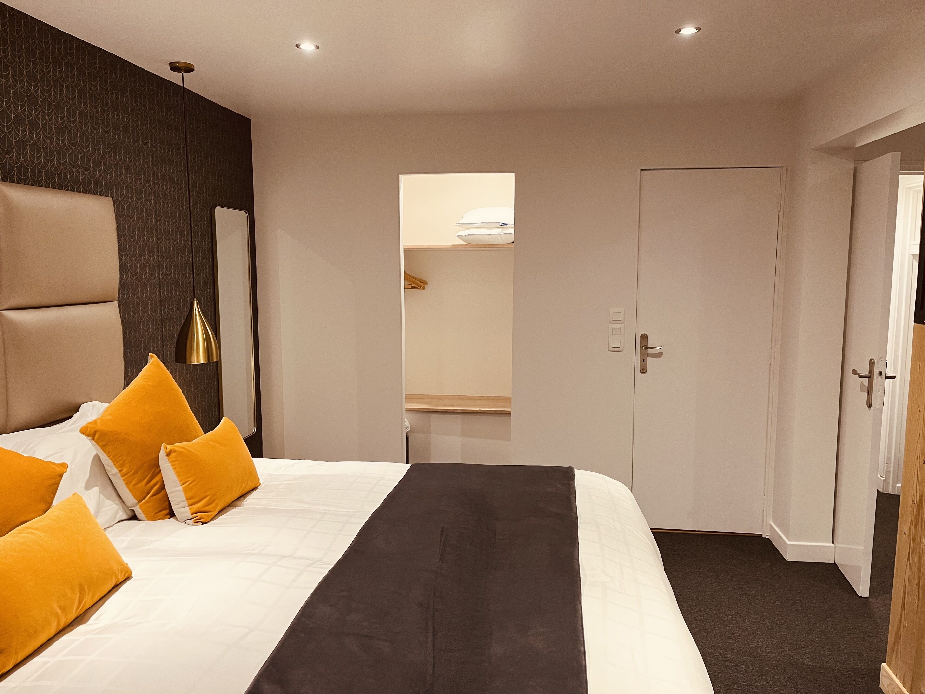A modern hotel room with a large bed, a bedside table, a wardrobe, and a mirror.