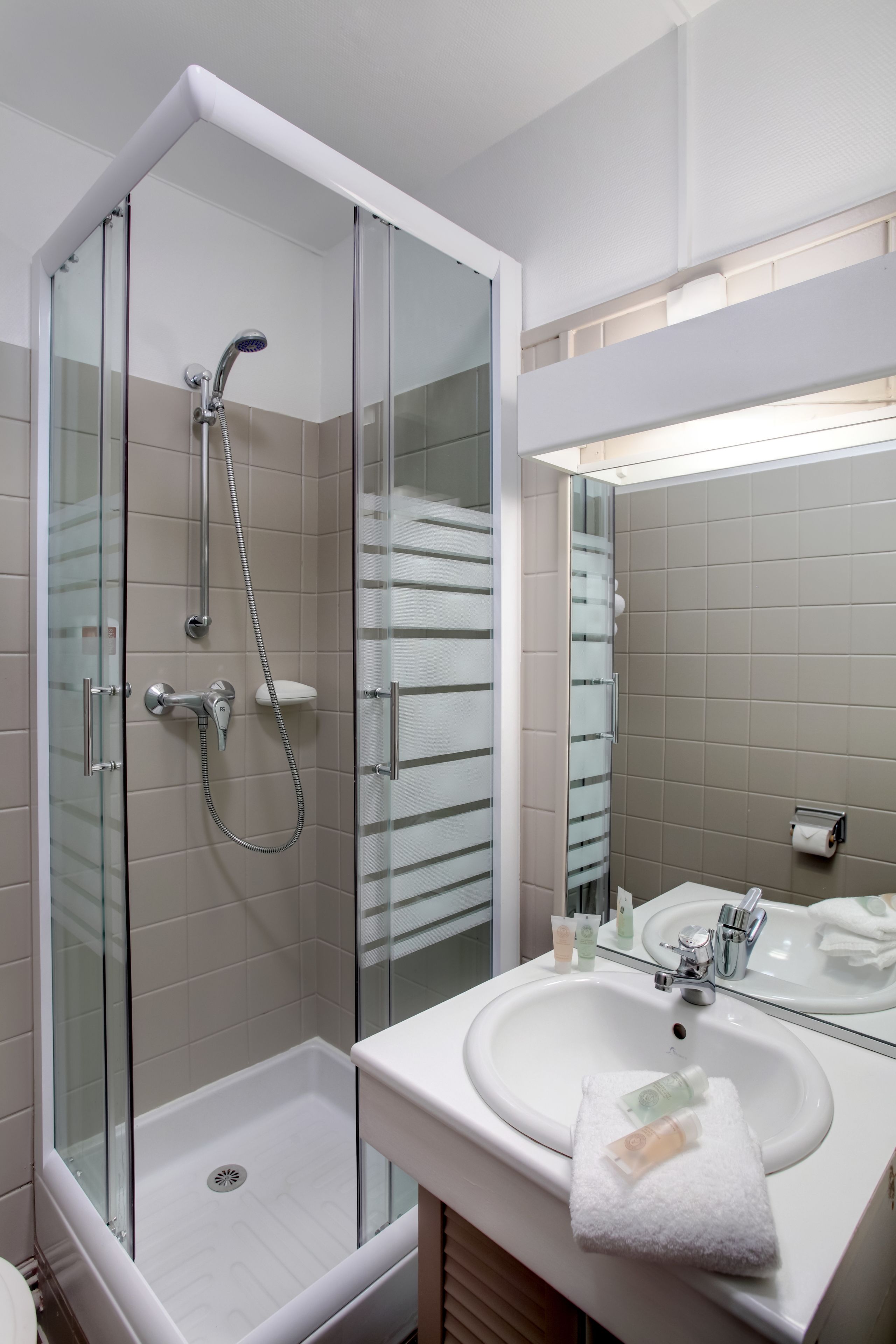 Un baño moderno con ducha envuelta en vidrio, un lavabo blanco y un espejo grande.