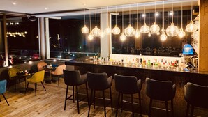 A bar area with multiple hanging light fixtures, a bar counter with various bottles, and several chairs. -  The Originals Boutique, Hôtel Le Panorama, Mont-Dore (Mont-Dore)