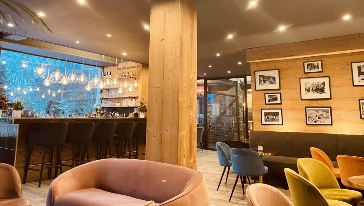 Un área de bar moderna con detalles de madera, una barra y un espacio de asientos con sillas coloridas.