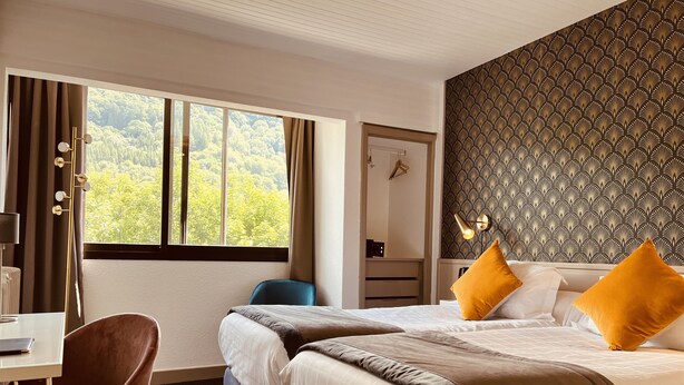 A hotel room with two beds, a desk, a chair, and a large window with a view of trees. -  The Originals Boutique, Hôtel Le Panorama, Mont-Dore (Mont-Dore)