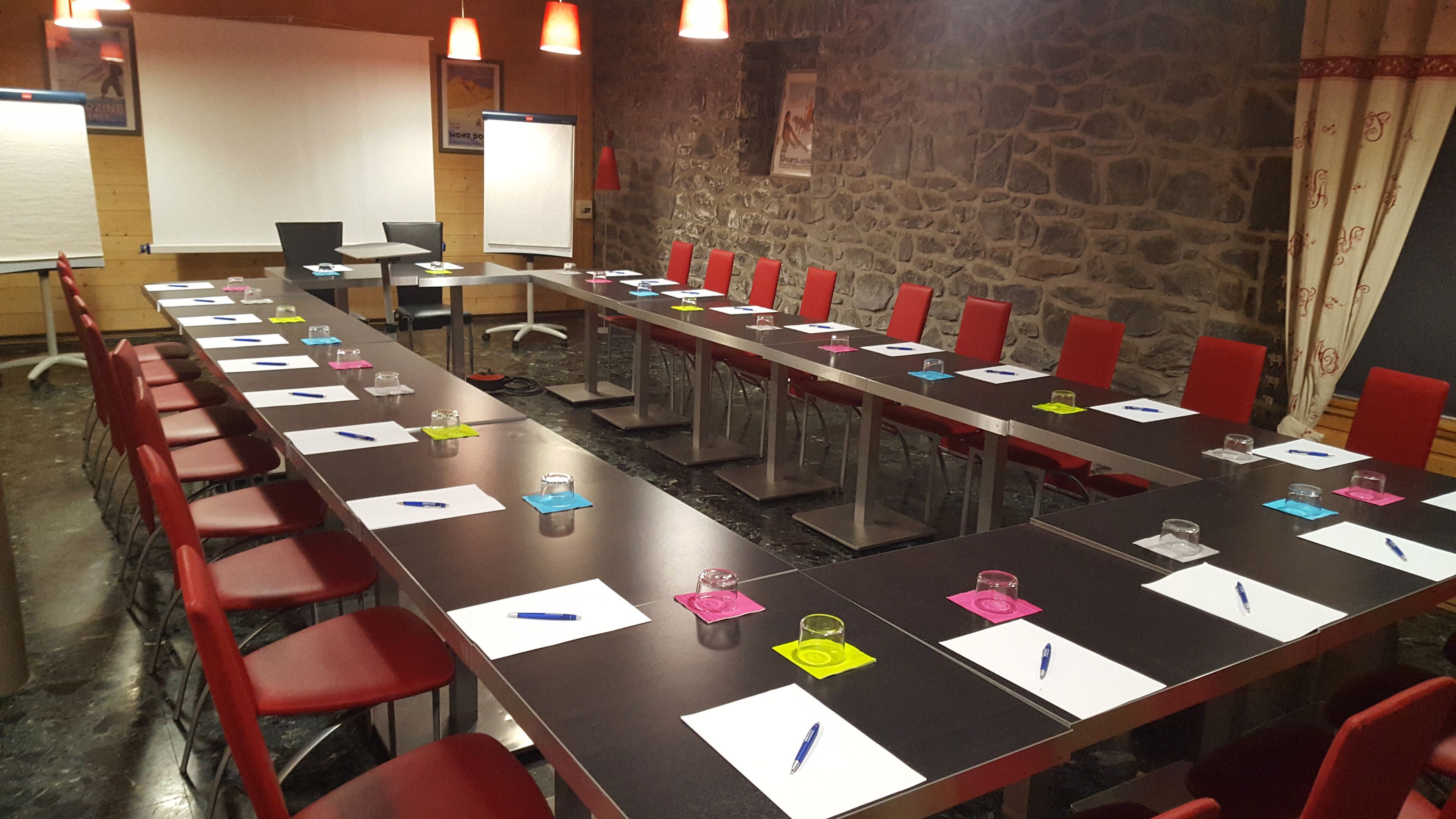Une salle de conférence avec une longue table, des chaises rouges et des tableaux blancs.