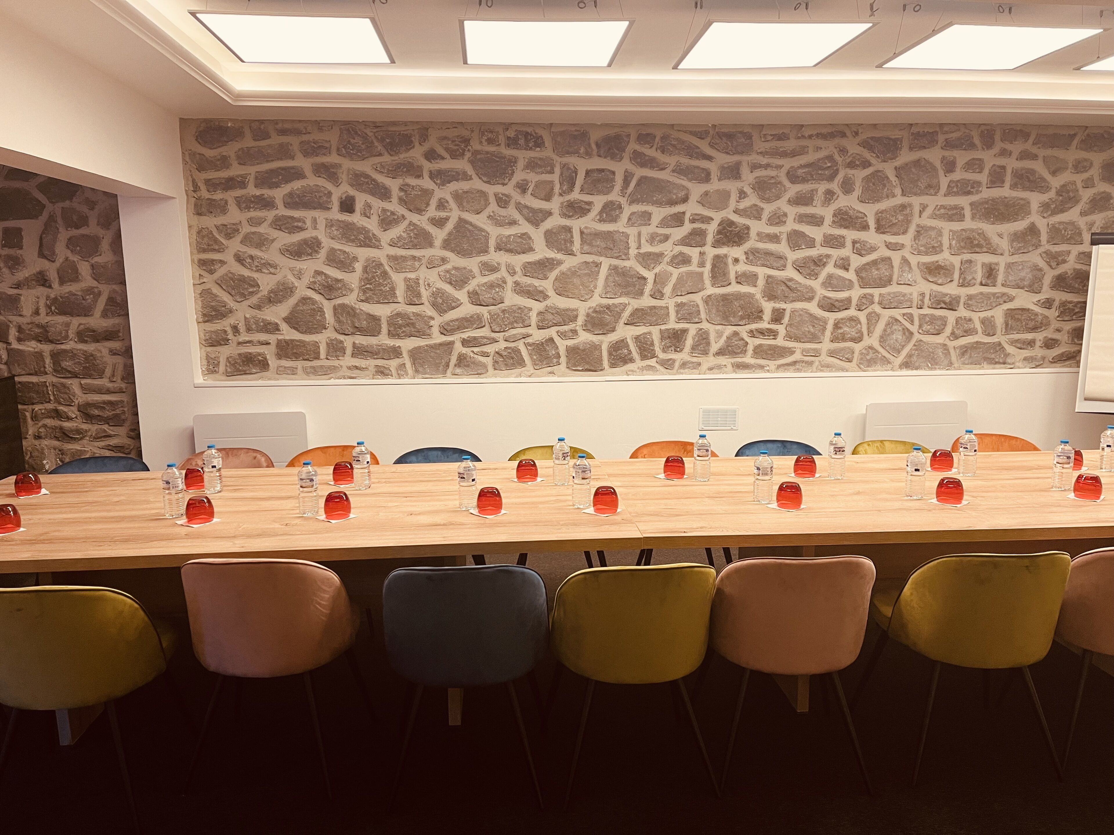 A conference room with a long table, colorful chairs, and water bottles.
