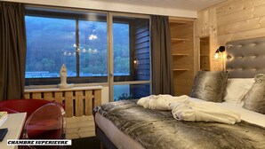 A bedroom with a large window, a bed with a fur-like cover, a red chair, and a wooden headboard. -  The Originals Boutique, Hôtel Le Panorama, Mont-Dore (Mont-Dore)