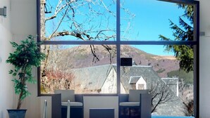 A clear indoor swimming pool with a view of a mountainous landscape through large windows. -  The Originals Boutique, Hôtel Le Panorama, Mont-Dore (Mont-Dore)