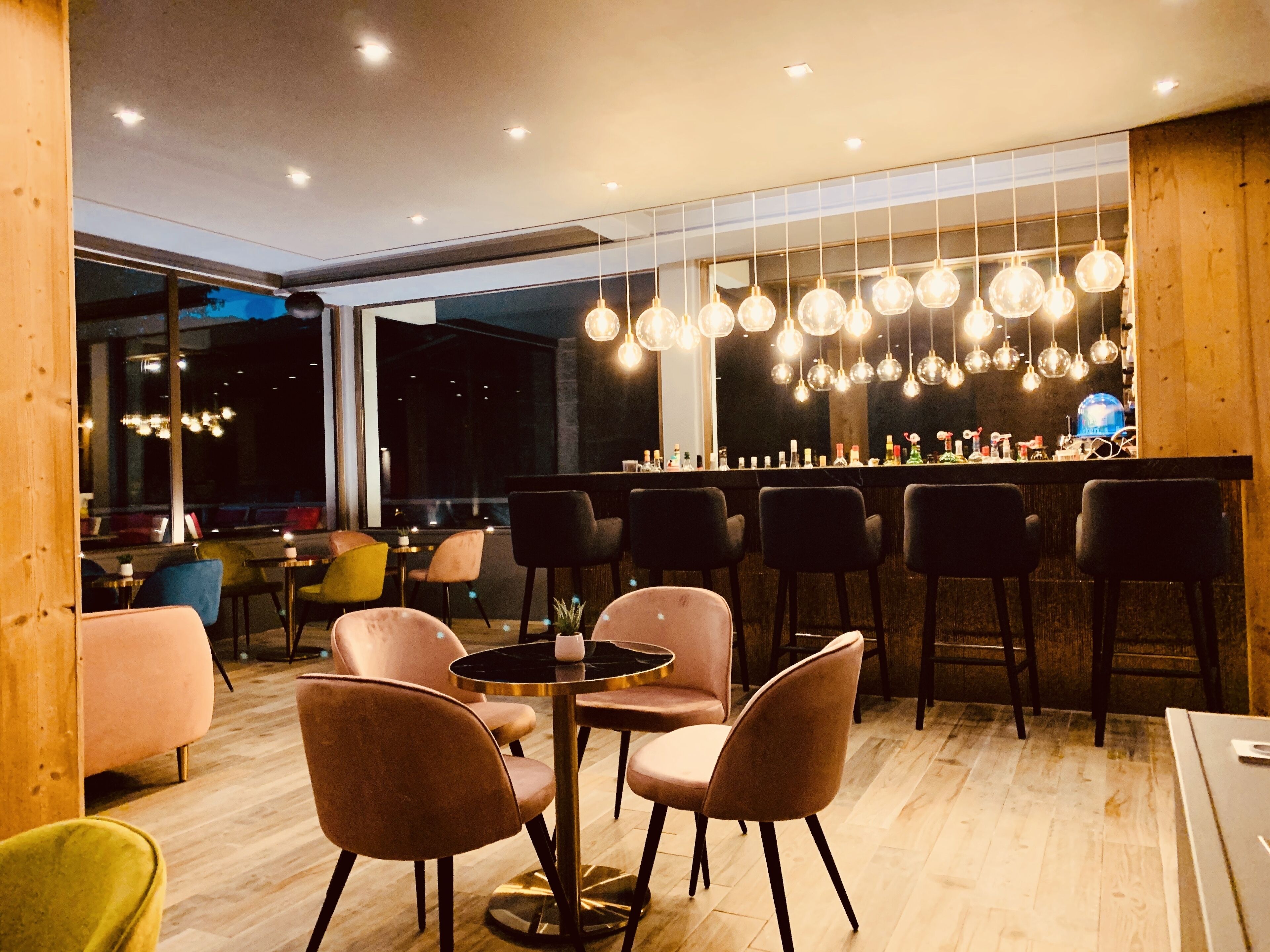 A modern bar area with round tables and chairs, hanging light fixtures, and a bar counter.