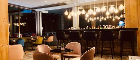 A modern bar area with round tables and chairs, hanging light fixtures, and a bar counter.