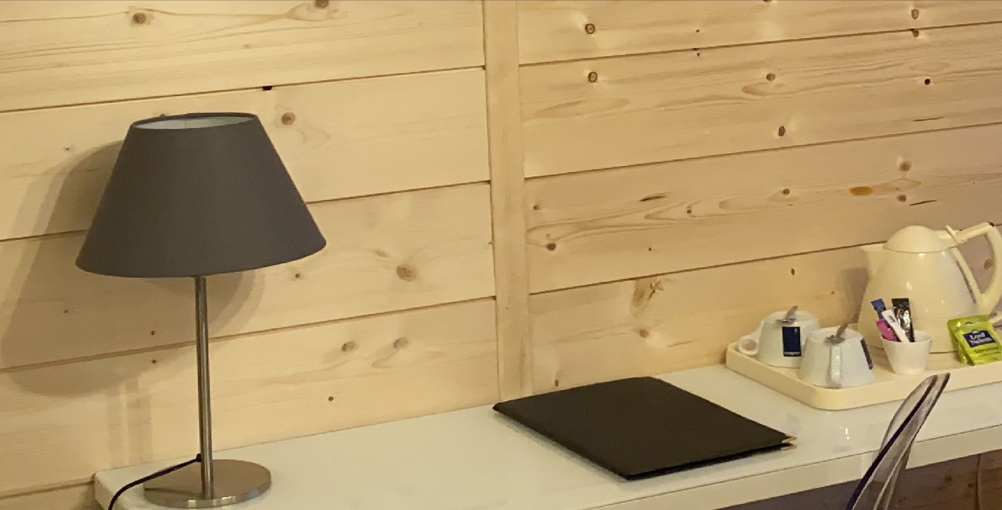 Een houten wand met een zwarte lamp, een witte dienblad met toiletartikelen en een zwart notitieboekje op een witte ondergrond.