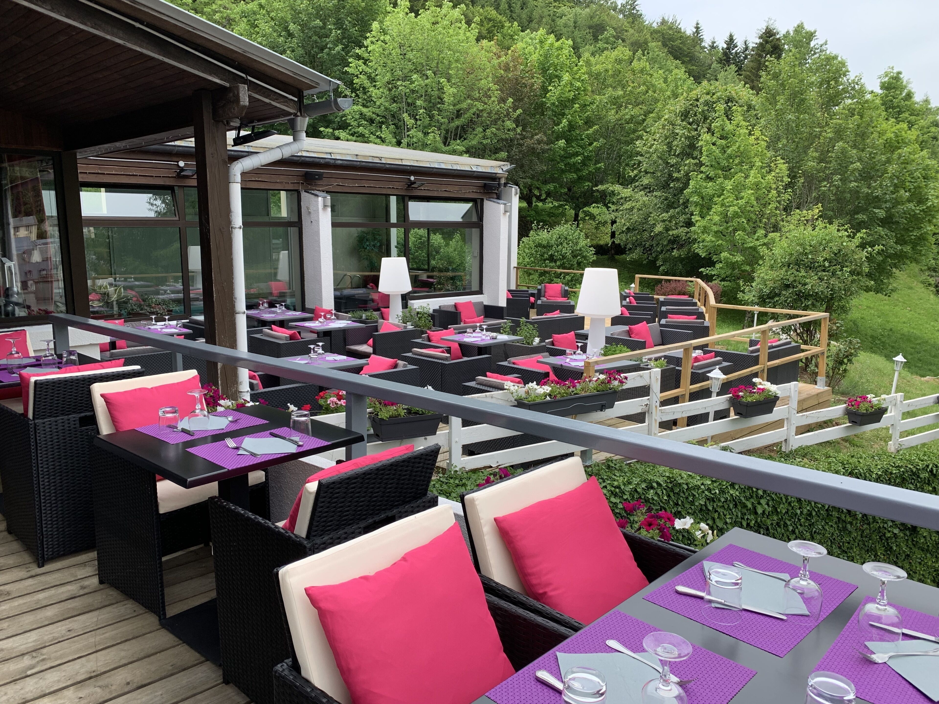Un área de comedor al aire libre con mobiliario de mimbre y manteles morados, rodeada de follaje.