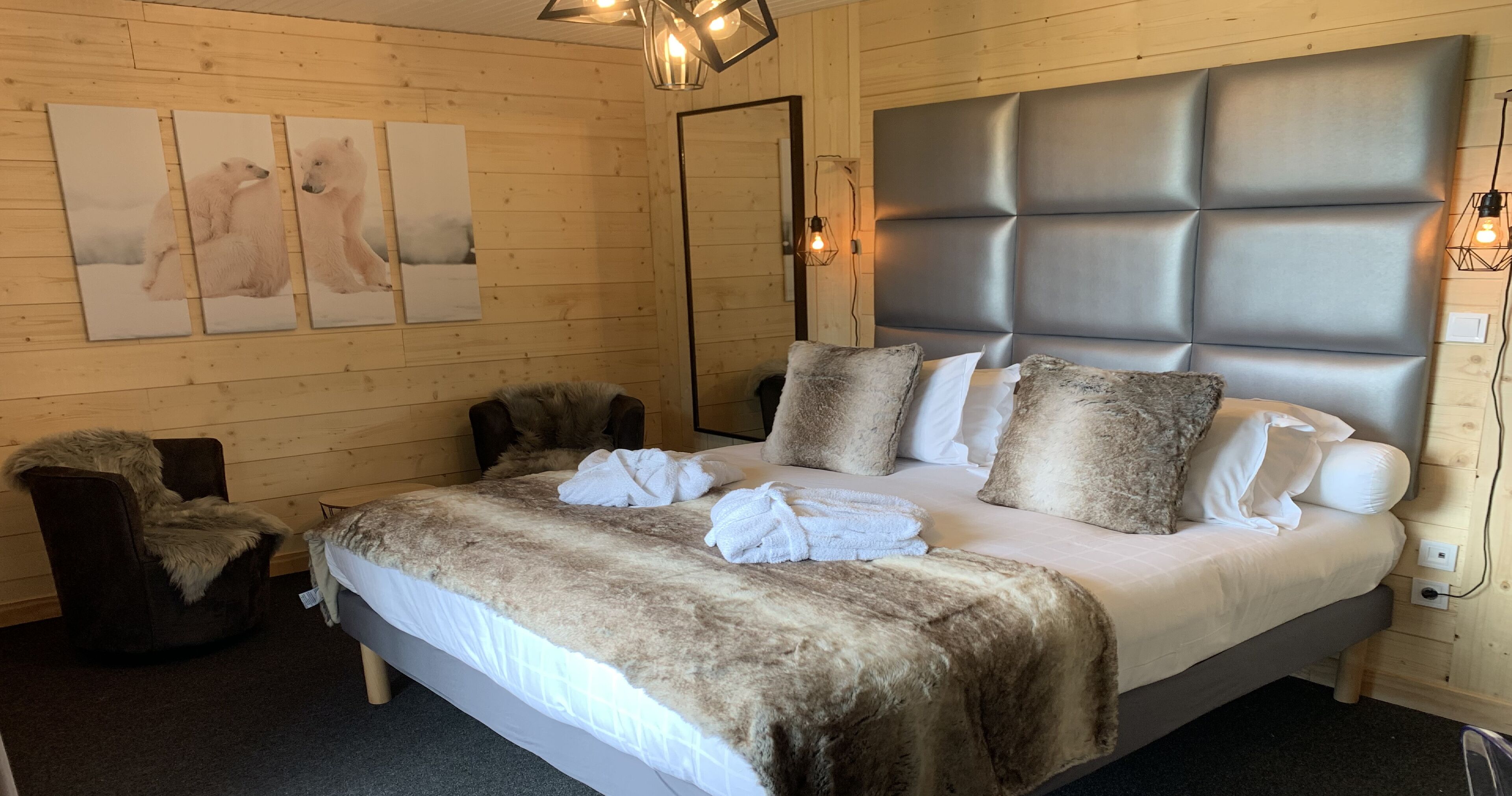 A bedroom with a large bed, a chair, and three wall-mounted paintings.