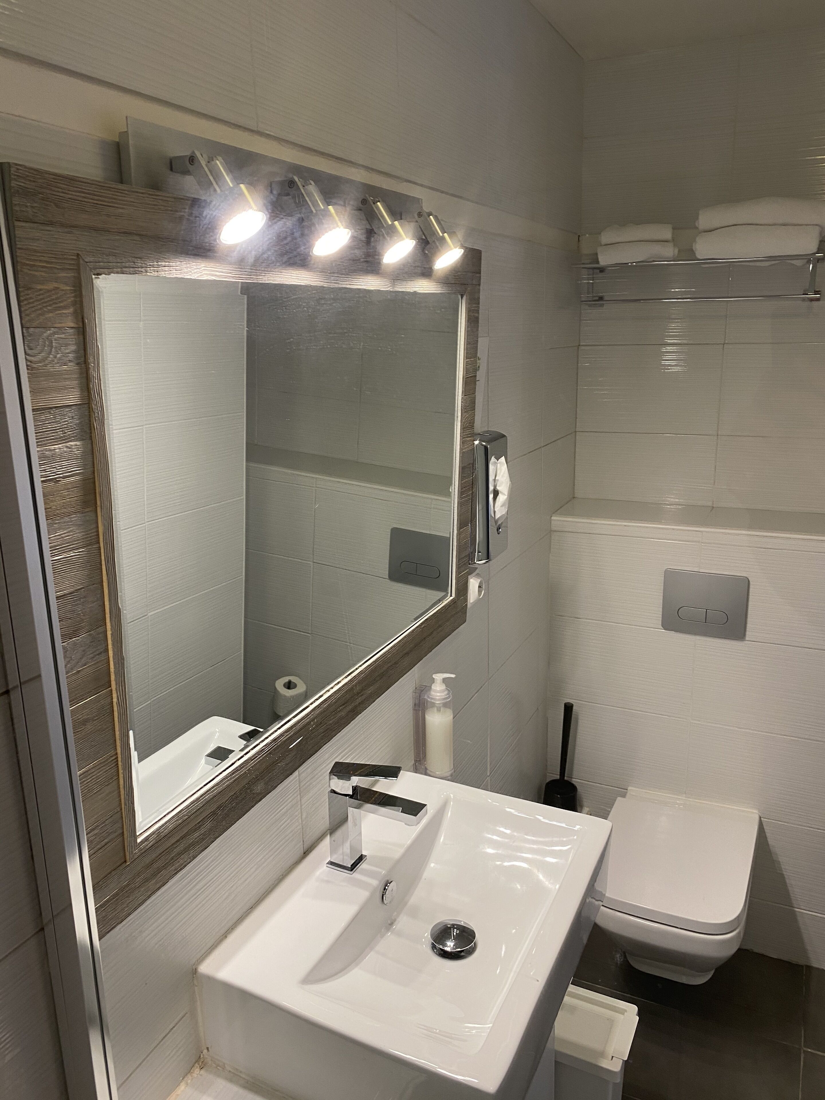 Un baño moderno con un espejo grande, un lavamanos blanco y un inodoro.