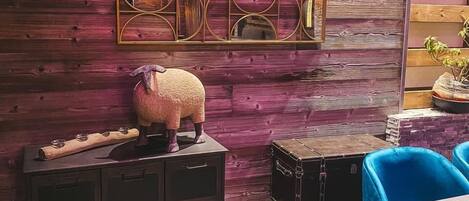 A wooden wall with a geometric mirror and a decorative sheep figure. There are two black suitcases and a blue chair.