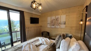 A bedroom with a large bed, a TV mounted on the wall, and a view of the outdoors. -  The Originals Boutique, Hôtel Le Panorama, Mont-Dore (Mont-Dore)