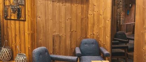 Un interior de madera con dos sillones grises tapizados, un cofre de madera y un televisor montado que muestra un mapa.