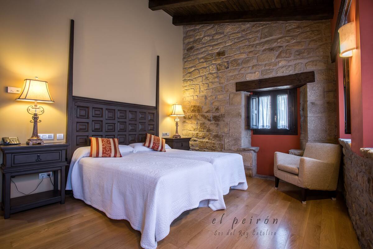 A hotel room with two beds, wooden floors, stone walls, and a stone fireplace.
