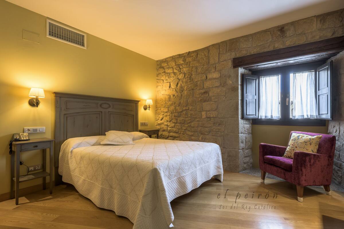 A bedroom with a bed, nightstands, a stone wall, a window, and a red chair.