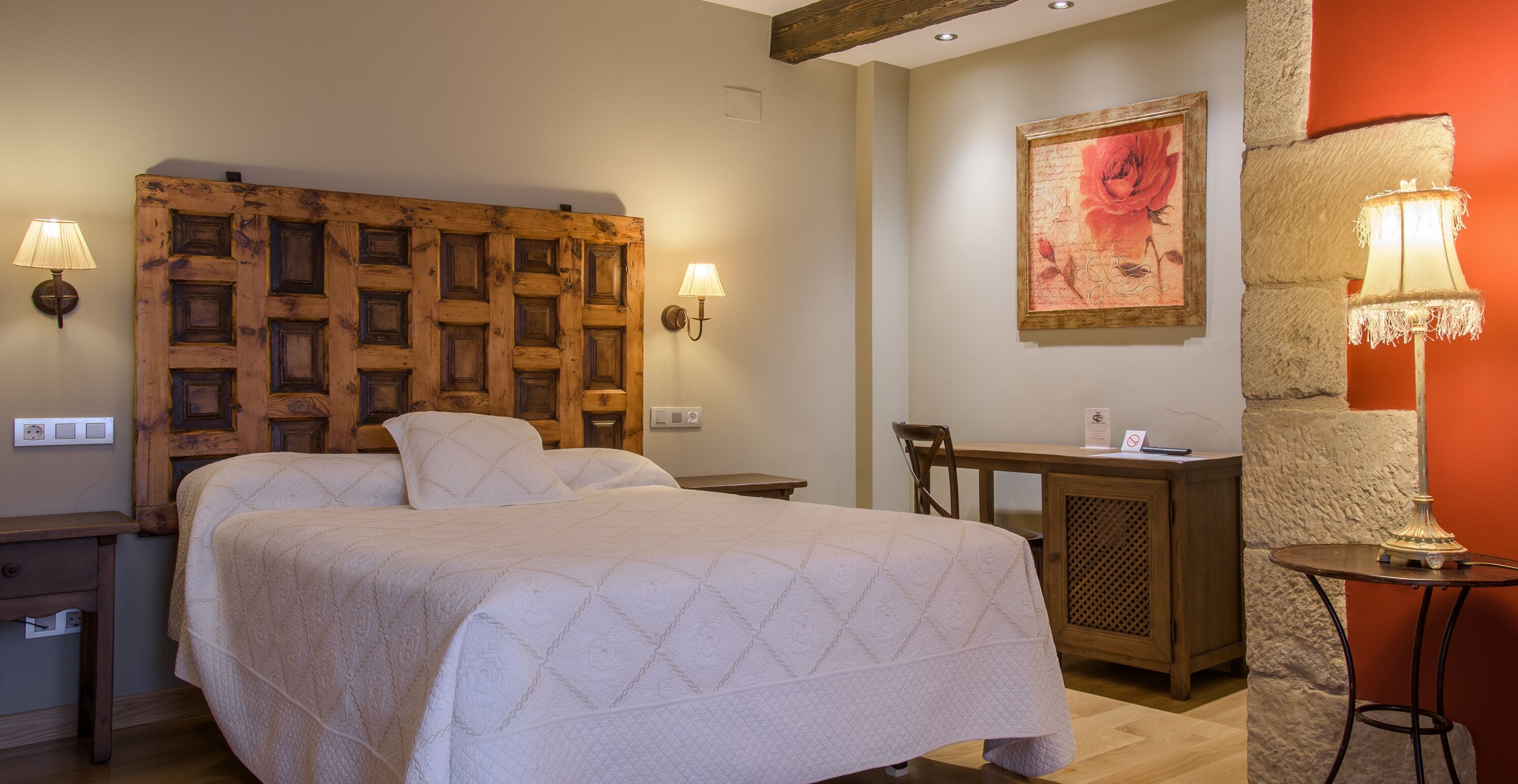 A bedroom with a wooden headboard, two bedside lamps, a desk, and a chair.