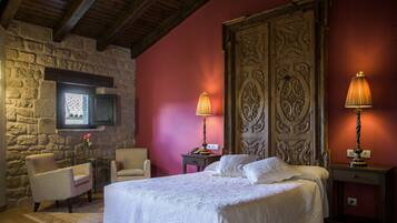 Um quarto acolhedor com parede de pedra, uma cama com roupa de cama branca, duas cadeiras e duas luminárias de cabeceira.