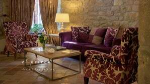 Uma sala de estar acolhedora com parede de pedra, sofá roxo, poltronas estampadas e uma mesa de centro com livros e um vaso.