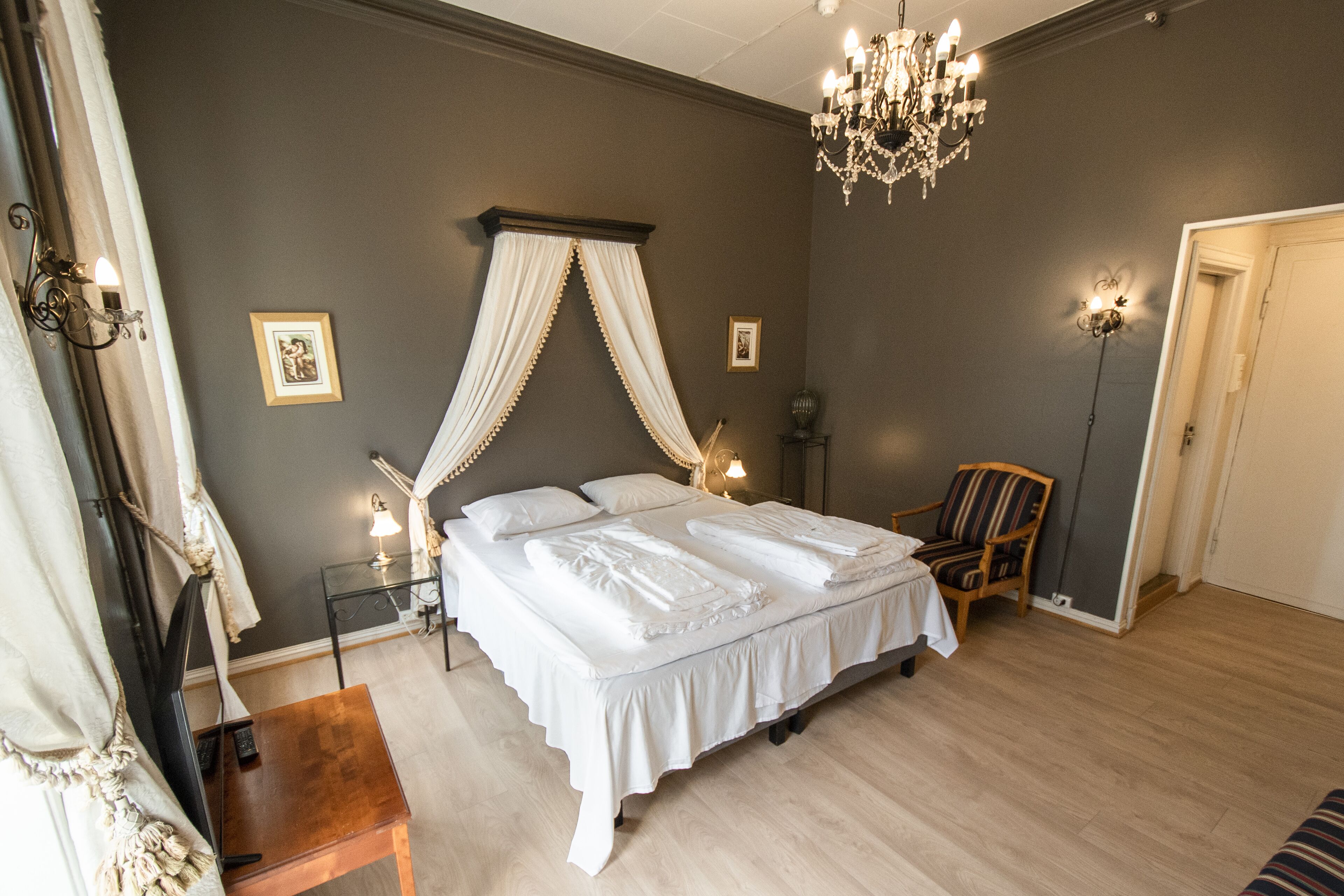 Un dormitorio con una cama con dosel, lámparas de noche, una silla de madera y una araña.