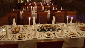 Ein formeller Speisesaal mit mehreren gedeckten Tischen, alle mit weißen Tischdecken, Kerzen und floralen Mittelpunkten.