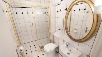 A bathroom with a glass-enclosed shower, a toilet, a sink, and a large mirror with a gold frame.