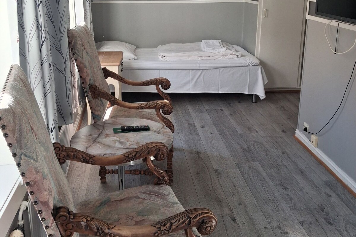 A bedroom with a bed, a chair, a painting, and a wardrobe.